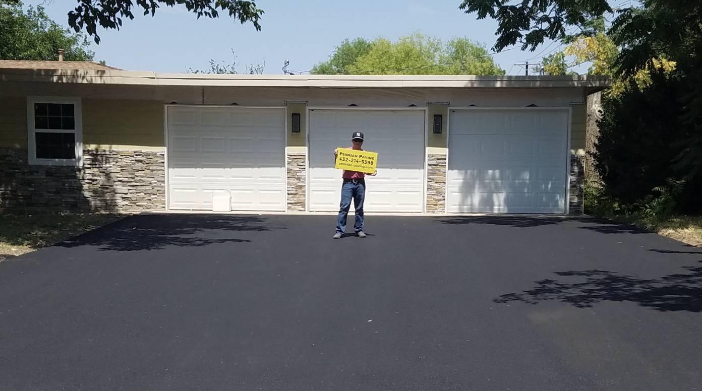 Permian Paving team member holding a company sign on a freshly paved residential driveway in Big Spring TX.