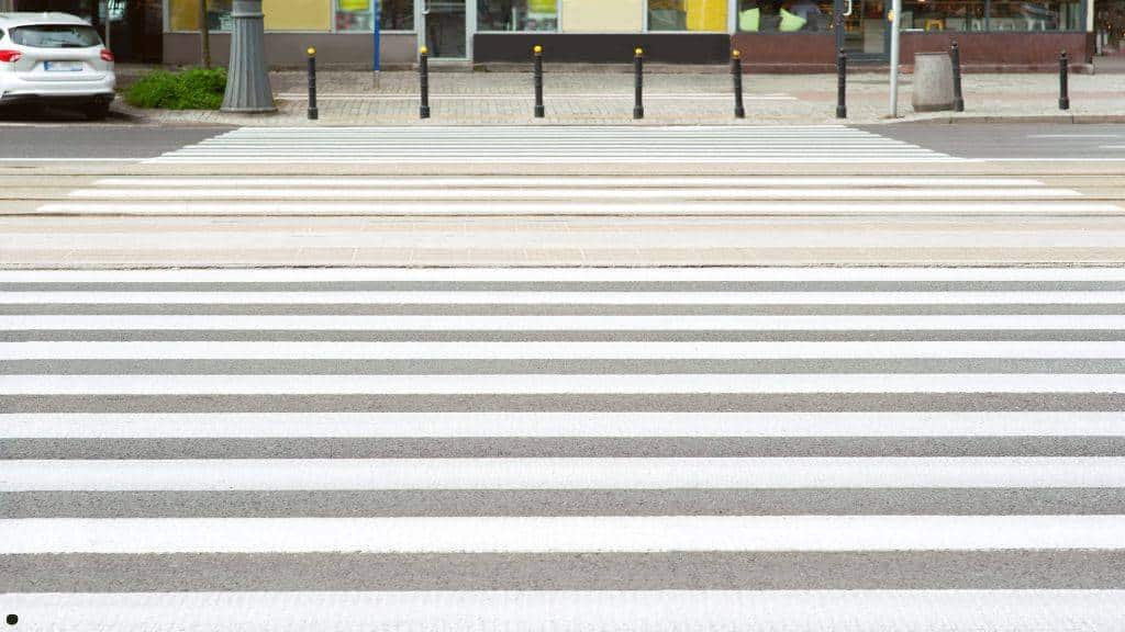 Newly painted white crosswalk stripes on a municipal asphalt road as part of seasonal city pavement upkeep